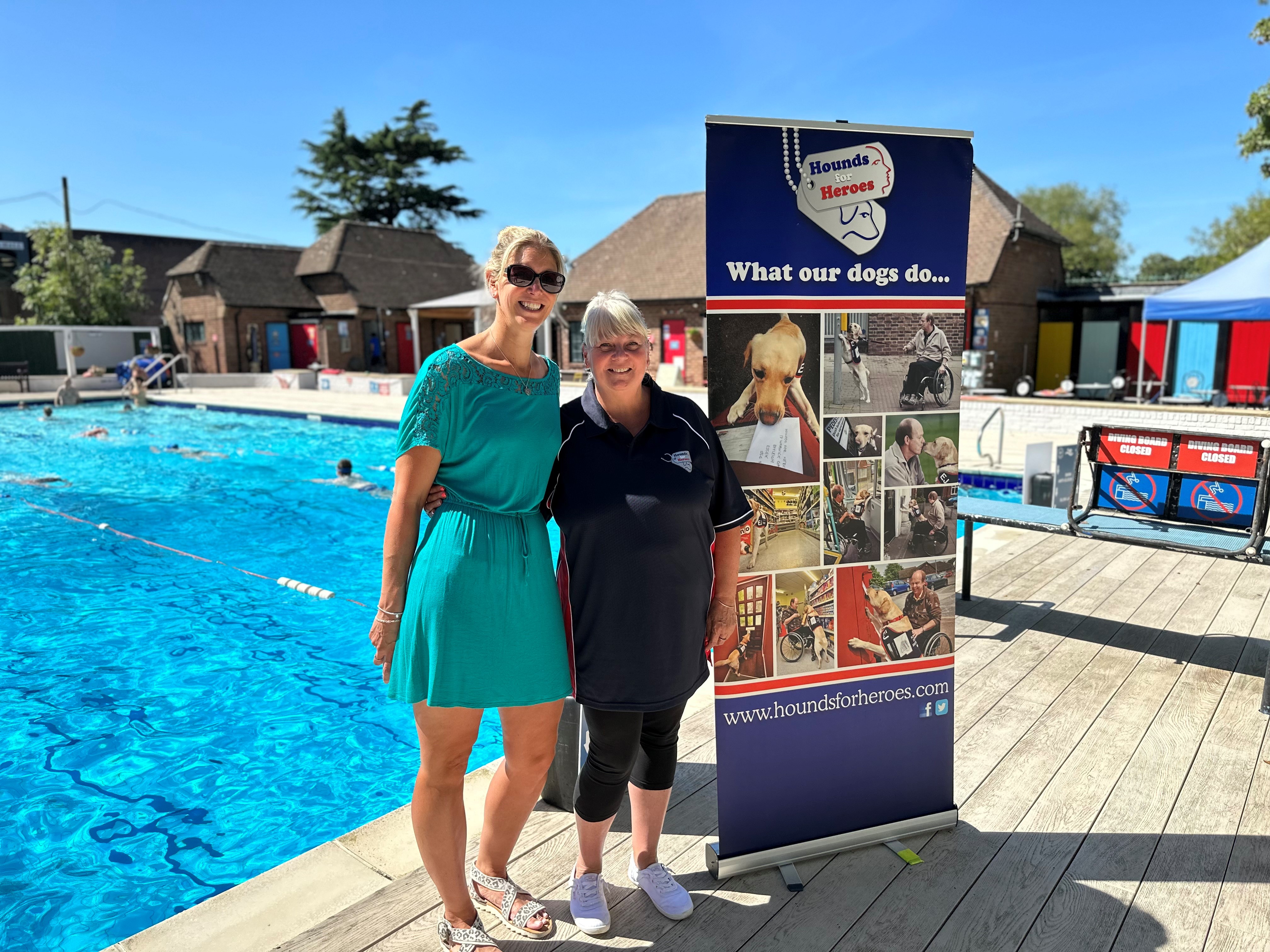 2 ladies by swimming pool by charity banner for Hounds for Heroes