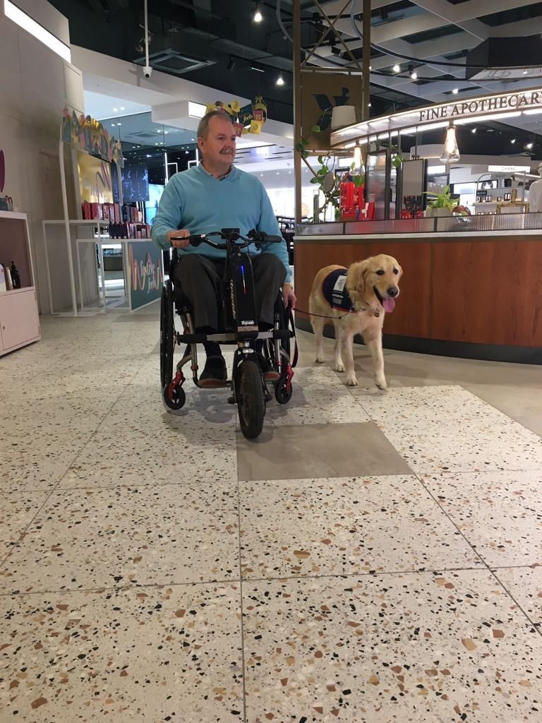 Man in an electric wheelchair in a shop with his assistance dog.
