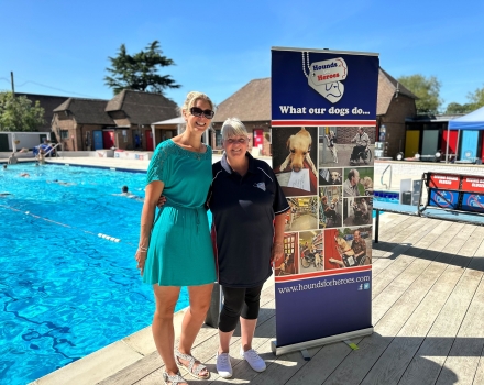 2 Ladies at an outdoor pool by charity banner for Hounds for Heroes